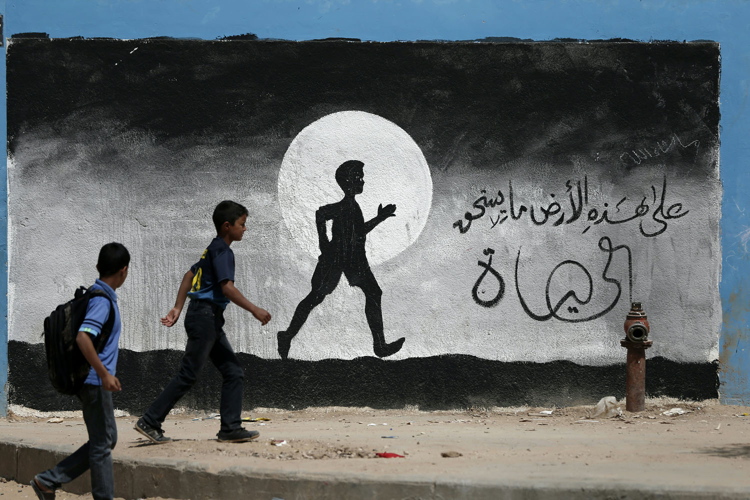 © Thomas Coex - AFP PHOTO - Photo éditée par Marina Passos - Elle représente deux écoliers palestiniens marchant le long d'un mur de l'école des Nations Unies de Beit Hanun, recouvert de graffitis, dans le Nord de la bande de Gaza le 9 mai 2016.