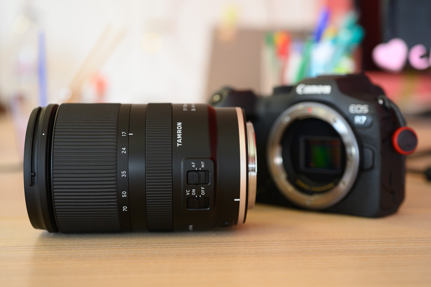 objectif Tamron 17-70 mm f/2,8 Di III-A VC RXD posé sur une table devant un boîtier Canon EOS R7